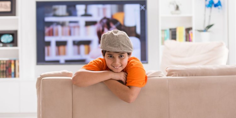 Dziecko siedzi samotnie w salonie z zegarem na ścianie i zamkniętymi drzwiami wejściowymi