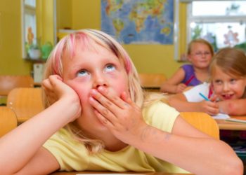 Uczeń w klasie szkolnej patrzy w telefon pod ławką inni skupieni na tablicy