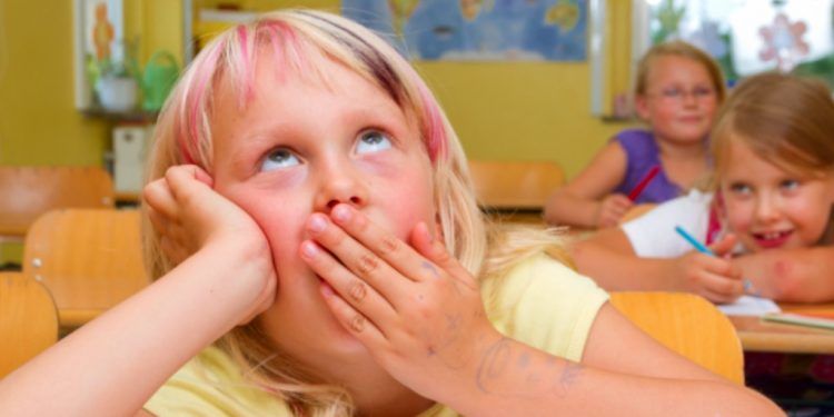 Uczeń w klasie szkolnej patrzy w telefon pod ławką inni skupieni na tablicy