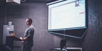 Biznesmen w garniturze z anielskimi skrzydłami ściska dłoń przedsiębiorcy przy stole z laptopem