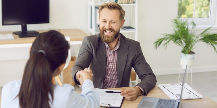 Młody przedsiębiorca podpisuje umowę pożyczki przy biurku z laptopem i planem biznesu