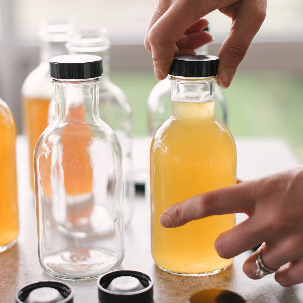 Rzęd butelek z różnokolorową kombuchą na półce w kuchni