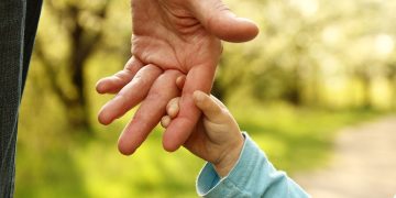 starszy dziadek tulący dwoje wnuków na kanapie w salonie