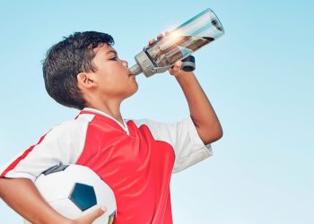 uśmiechnięta kobieta trzymająca szklankę wody z plasterkiem cytryny na stole