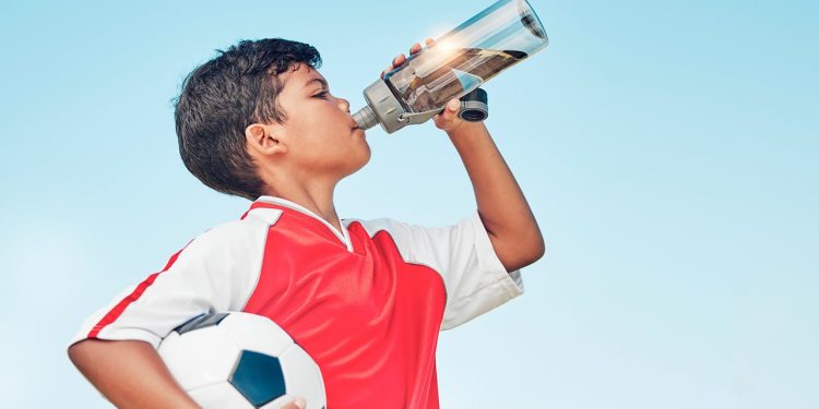 uśmiechnięta kobieta trzymająca szklankę wody z plasterkiem cytryny na stole